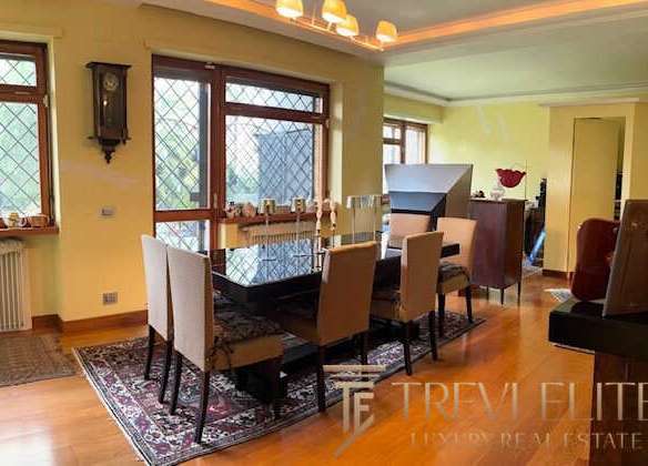 Модный интерьер столовой комнаты с большим деревенским столом и уютными стульями, окруженными большими окнами с видом на природу, создающими светлую и просторную атмосферу.