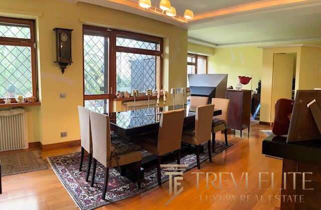 Модный интерьер столовой комнаты с большим деревенским столом и уютными стульями, окруженными большими окнами с видом на природу, создающими светлую и просторную атмосферу.