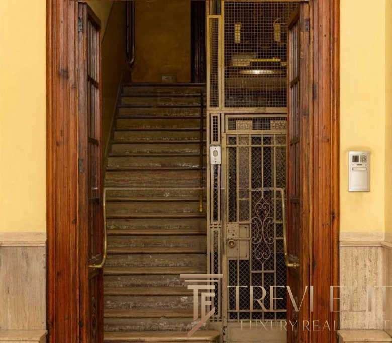 Изображение старой лестницы в жилом доме, окруженной деревянными дверями и металлическими дверцами на лифтовой шахте, внутри уютного интерьера.
