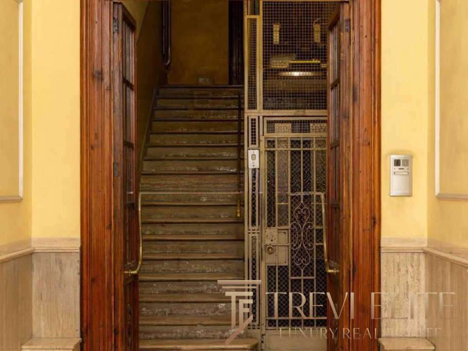 Изображение старой лестницы в жилом доме, окруженной деревянными дверями и металлическими дверцами на лифтовой шахте, внутри уютного интерьера.