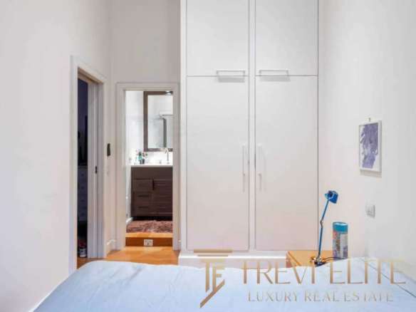 Элегантная спальня с белыми стенами, встроенными шкафами и прикроватной тумбочкой, создающая уютную атмосферу в высококлассной недвижимости.