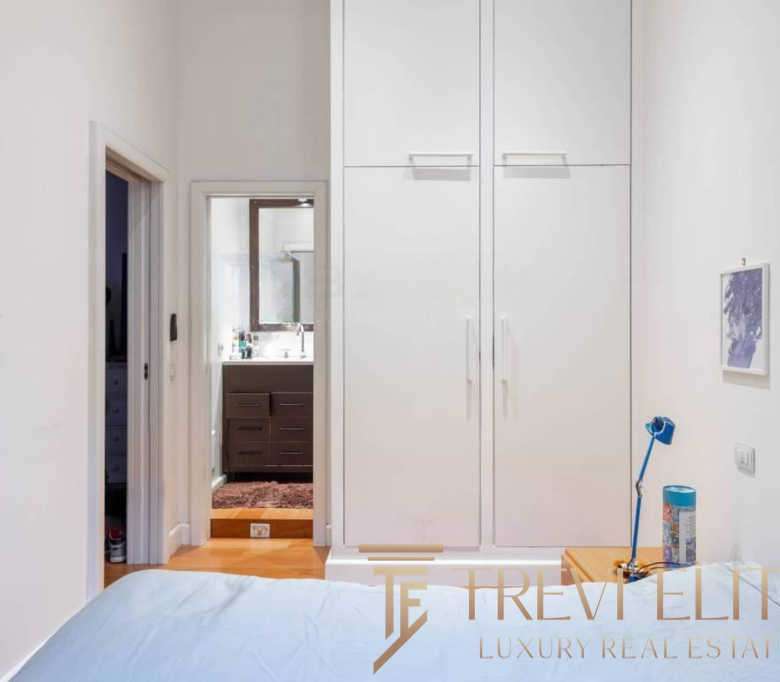 Элегантная спальня с белыми стенами, встроенными шкафами и прикроватной тумбочкой, создающая уютную атмосферу в высококлассной недвижимости.