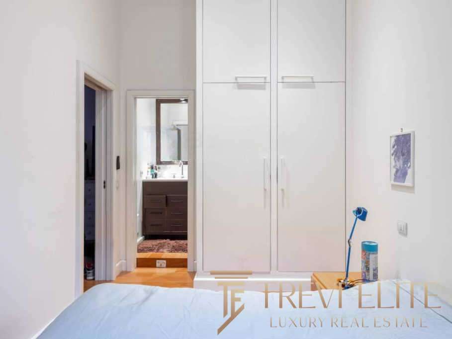 Элегантная спальня с белыми стенами, встроенными шкафами и прикроватной тумбочкой, создающая уютную атмосферу в высококлассной недвижимости.