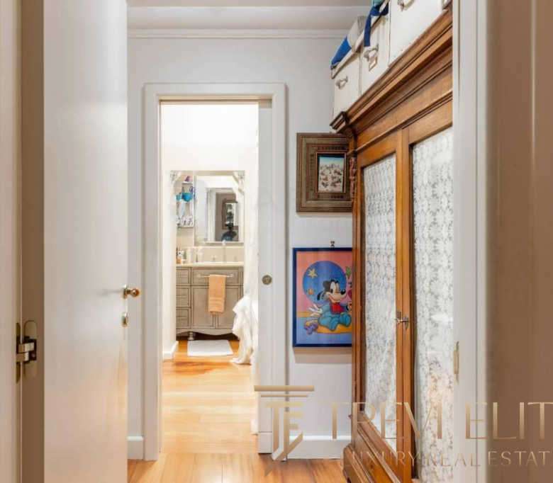 Просторый коридор с деревянной мебелью и яркими картинами в уютной квартире высокого класса. Вид в ванную комнату с светлым интерьером и дубовыми полами, создающими комфортную атмосферу.