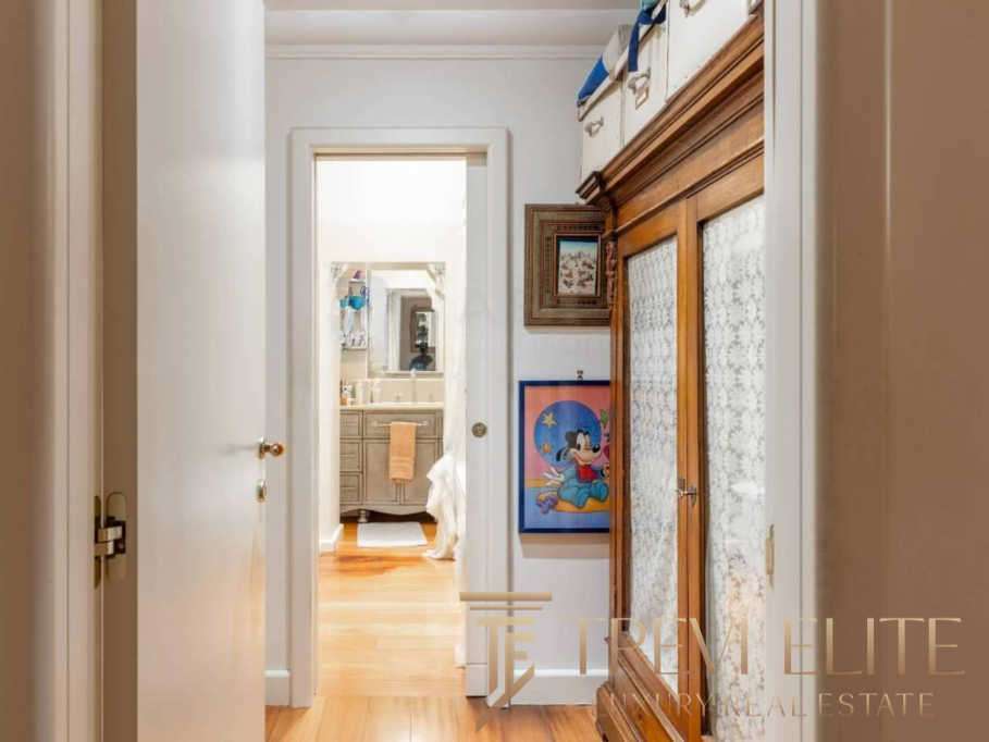 Просторый коридор с деревянной мебелью и яркими картинами в уютной квартире высокого класса. Вид в ванную комнату с светлым интерьером и дубовыми полами, создающими комфортную атмосферу.