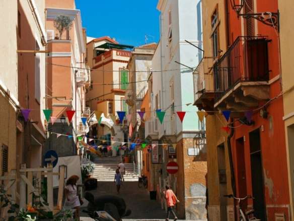 Красочная улица в Италии с яркими домами и праздничными флажками, создающая атмосферу уюта и живописности. Идеальное место для инвестиций в элитную недвижимость.