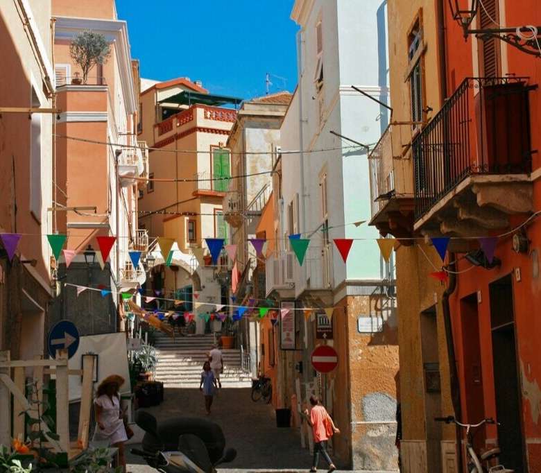 Красочная улица в Италии с яркими домами и праздничными флажками, создающая атмосферу уюта и живописности. Идеальное место для инвестиций в элитную недвижимость.