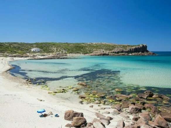 Великолепный пляж на берегу с прозрачной бирюзовой водой, песчаным побережьем и скалами, окруженными зеленью и бескрайним синим небом, идеальное место для отдыха и наслаждения природой.