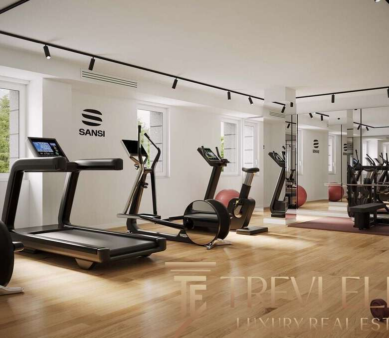 Современный фитнес-зал в элитном жилом комплексе с тренажёрами и зоной для йоги, просторная комната с большим количеством естественного света и стильным дизайном.