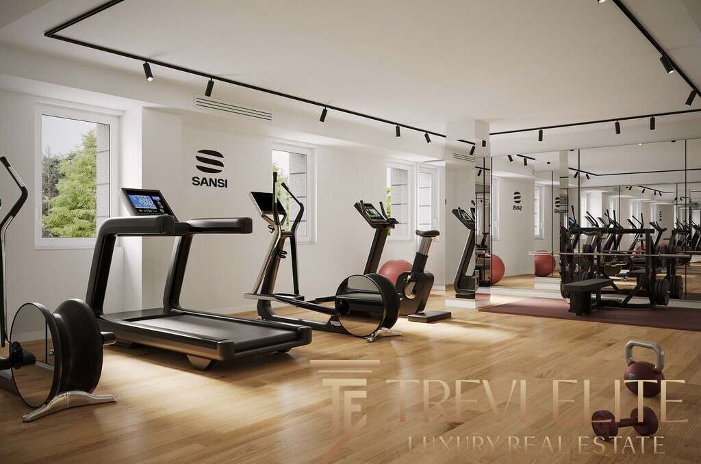 Современный фитнес-зал в элитном жилом комплексе с тренажёрами и зоной для йоги, просторная комната с большим количеством естественного света и стильным дизайном.