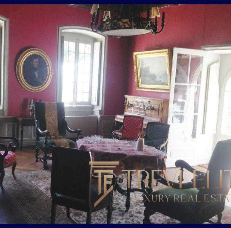 Уютная гостиная в классическом стиле с антикварной мебелью, ярко-красными стенами и большими окнами с естественным освещением, украшенная картинами и светильниками, идеально подходит для элитной недвижимости.