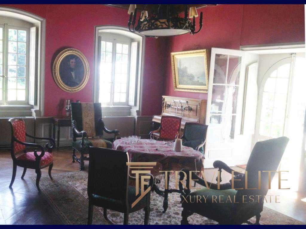 Уютная гостиная в классическом стиле с антикварной мебелью, ярко-красными стенами и большими окнами с естественным освещением, украшенная картинами и светильниками, идеально подходит для элитной недвижимости.