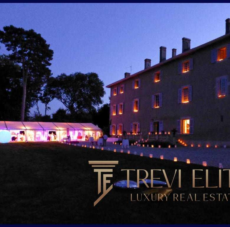 Элегантное ночное изображение роскошного особняка с подсвеченными окнами и зоной для мероприятий под звездным небом, рекламирующее агентство недвижимости Треви Элит.