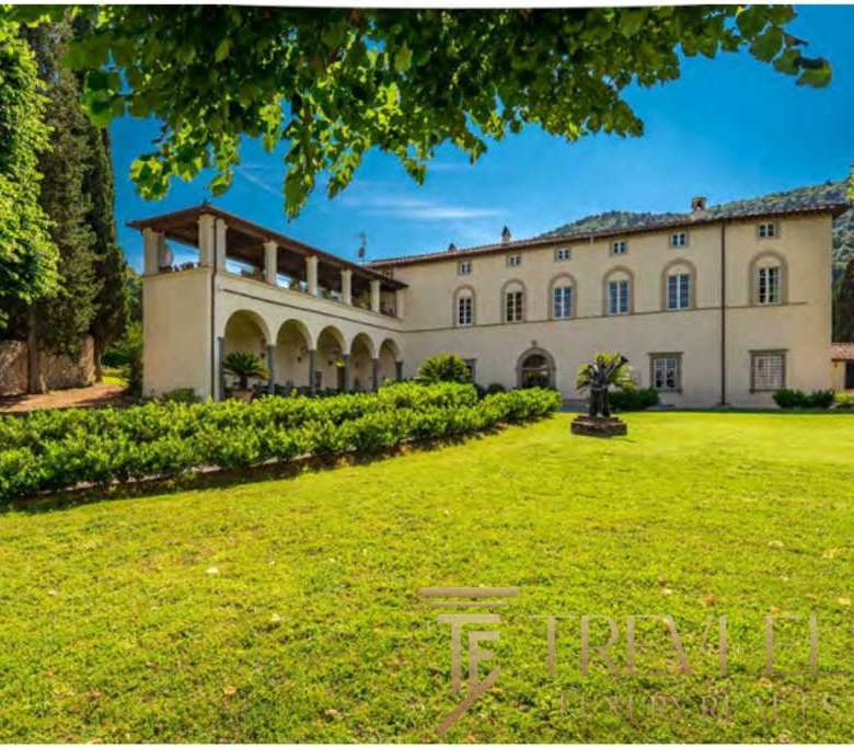 Роскошное итальянское особняк на зеленом лугу, окруженный садами и древними деревьями, под ярким голубым небом, идеальный дом для ценителей элитной недвижимости.