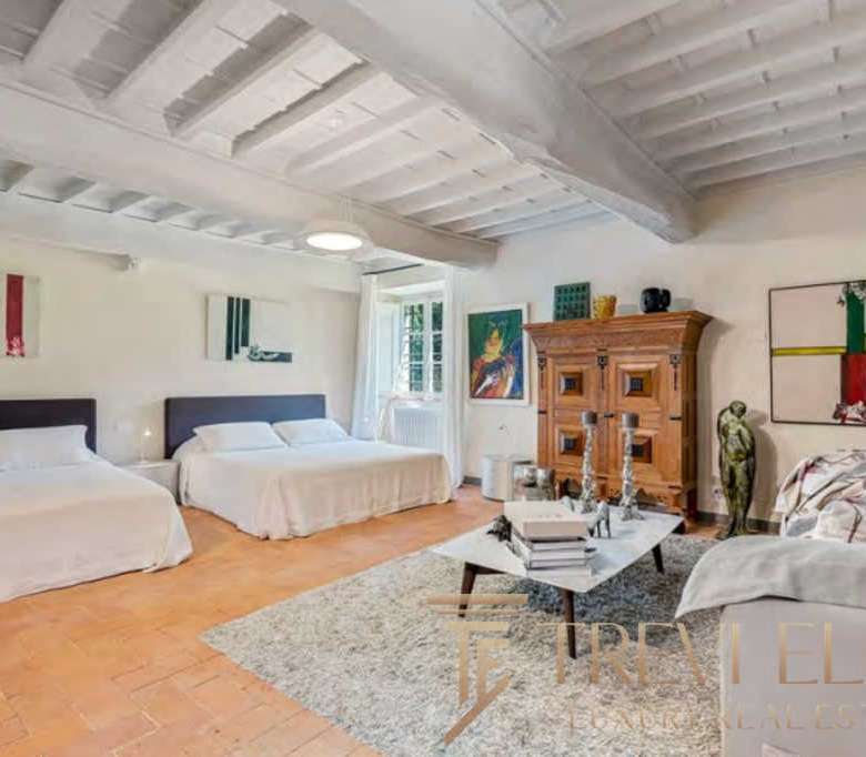 Изображение роскошной гостиной с белыми стенами, деревянной мебелью и уютным интерьером, предлагающее престижную недвижимость в Италии и мире.