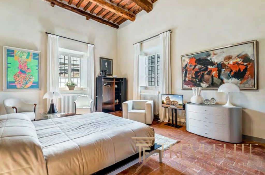 Элегантная спальня в роскошной итальянской недвижимости, светлый интерьер с живописными произведениями искусства и уютной атмосферой, идеальное жилье для ценителей эксклюзивных объектов.