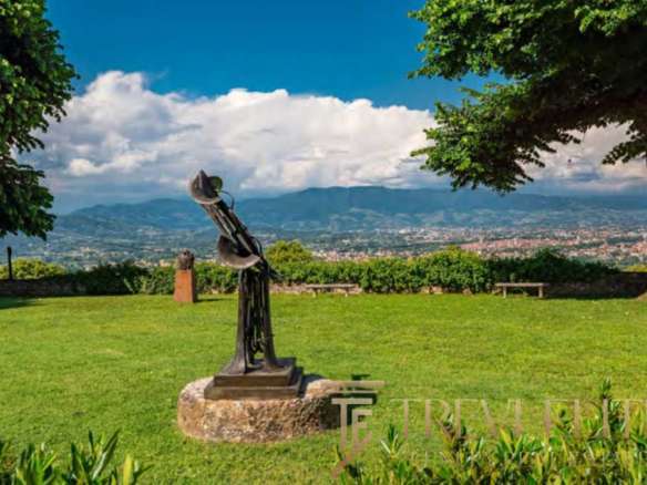 Современная скульптура на лужайке с панорамным видом на горы и город, зеленые деревья и чистое небо, расположен в элитной недвижимостной зоне Италии, эксклюзивное агентство Треви Элит.