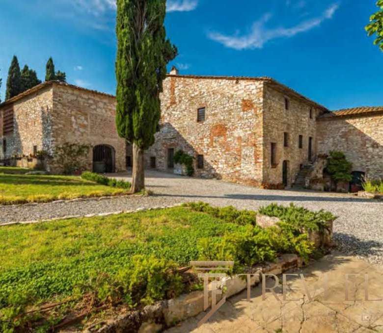 Средневековая каменная усадьба в живописной итальянской деревушке, окруженная зеленью и грациозными деревьями, под ярким небом и солнечным светом.