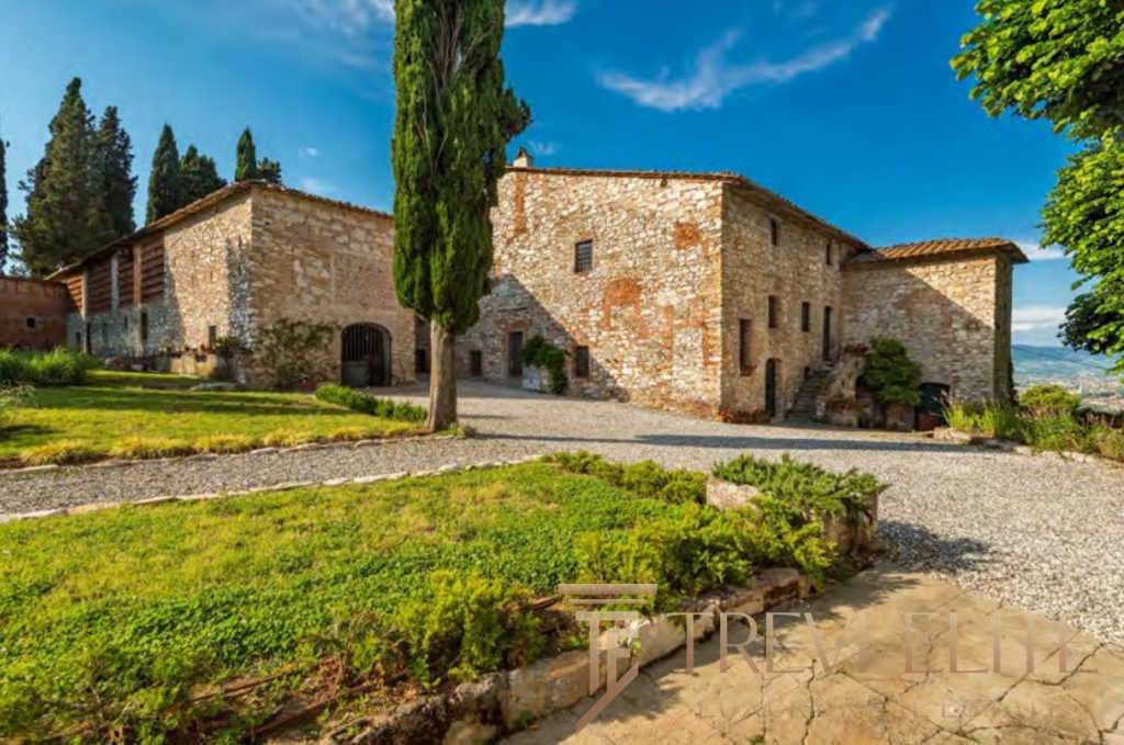 Средневековая каменная усадьба в живописной итальянской деревушке, окруженная зеленью и грациозными деревьями, под ярким небом и солнечным светом.