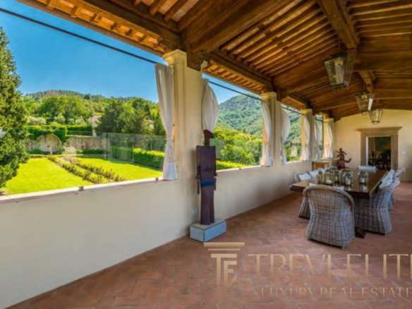 Уютная терраса с видом на зеленый сад и горы, идеально подходит для отдыха и наслаждения природой, выполнена в традиционном стиле с деревянным потолком и декоративными элементами.