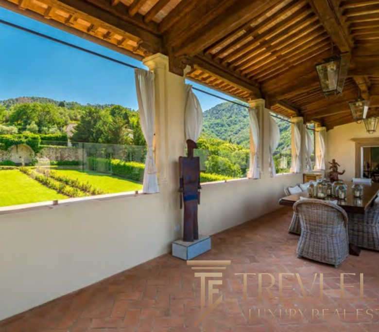 Уютная терраса с видом на зеленый сад и горы, идеально подходит для отдыха и наслаждения природой, выполнена в традиционном стиле с деревянным потолком и декоративными элементами.