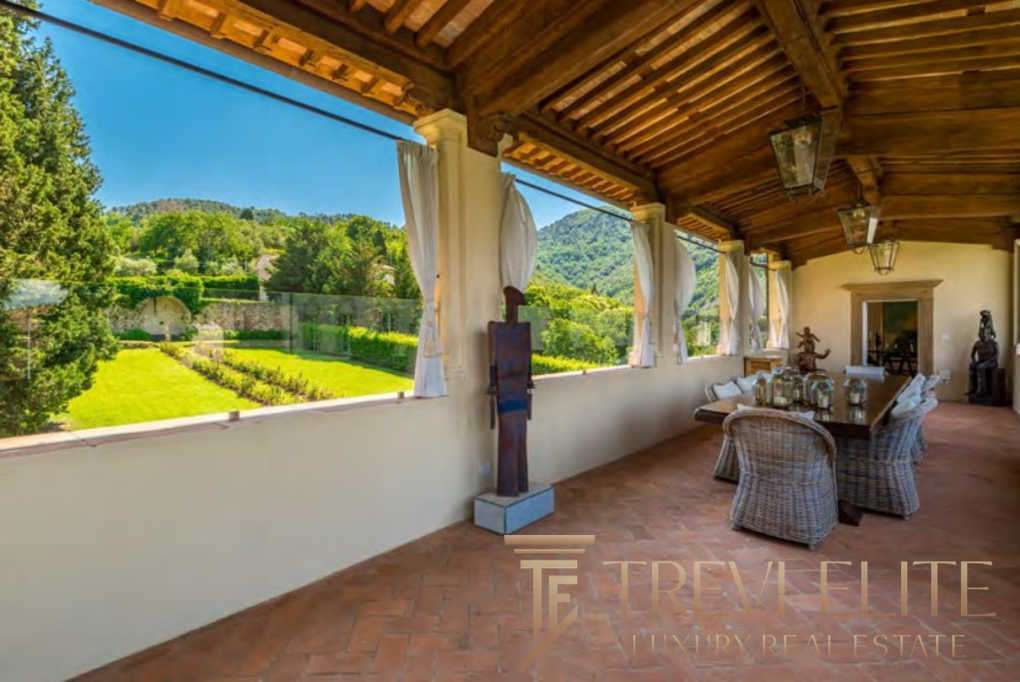 Уютная терраса с видом на зеленый сад и горы, идеально подходит для отдыха и наслаждения природой, выполнена в традиционном стиле с деревянным потолком и декоративными элементами.