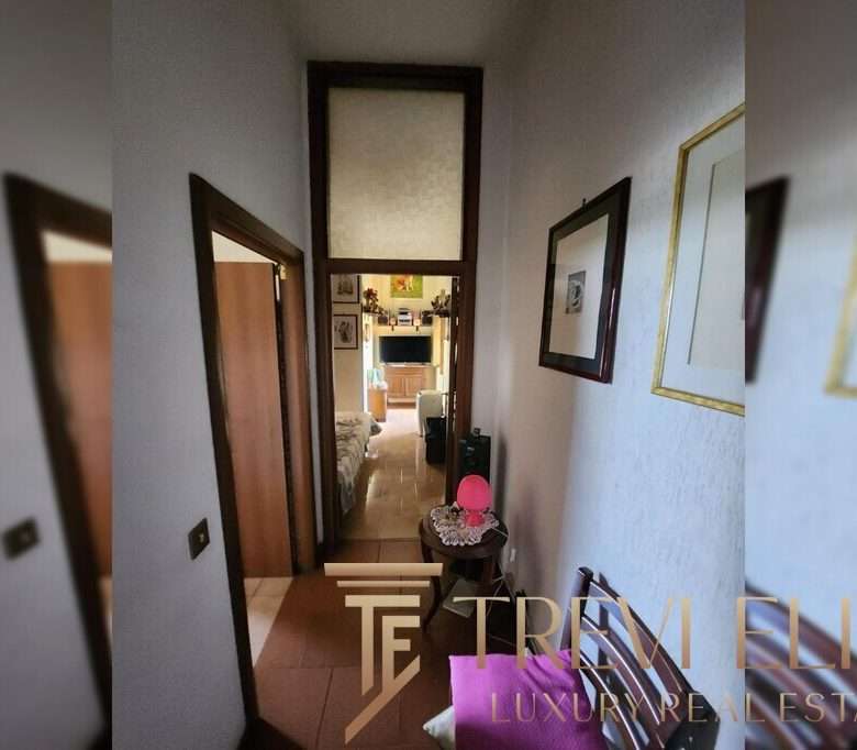 Узкая прихожая с рамками картин на стене, ведущая к жилой комнате с телевизором, создающая уютную атмосферу в роскошной недвижимости.