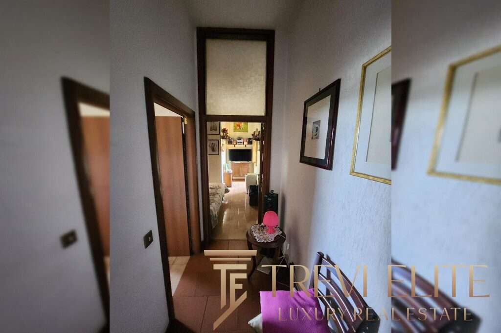 Узкая прихожая с рамками картин на стене, ведущая к жилой комнате с телевизором, создающая уютную атмосферу в роскошной недвижимости.