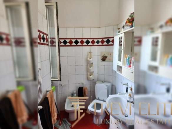 Бумажные полотенца на стене, зеркало, писсуар и раковина в небольшой ванной комнате с белыми плитками и красно-черной декоративной полостью.