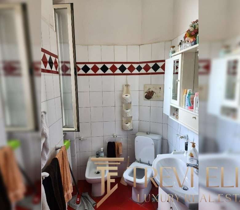 Бумажные полотенца на стене, зеркало, писсуар и раковина в небольшой ванной комнате с белыми плитками и красно-черной декоративной полостью.