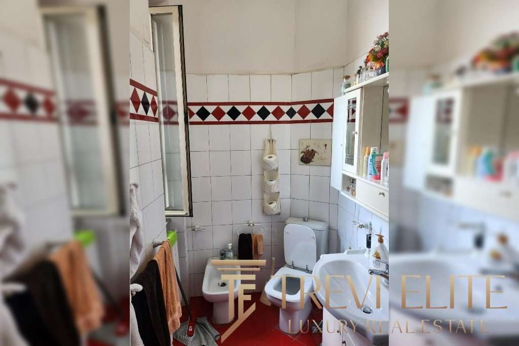 Бумажные полотенца на стене, зеркало, писсуар и раковина в небольшой ванной комнате с белыми плитками и красно-черной декоративной полостью.