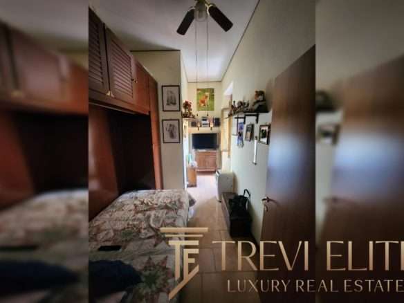 Уютная комната с деревянной мебелью и телевизором, оформление в домашних стилях, фотографии и картины на стенах, светлый интерьер, подходящий для комфортного проживания.