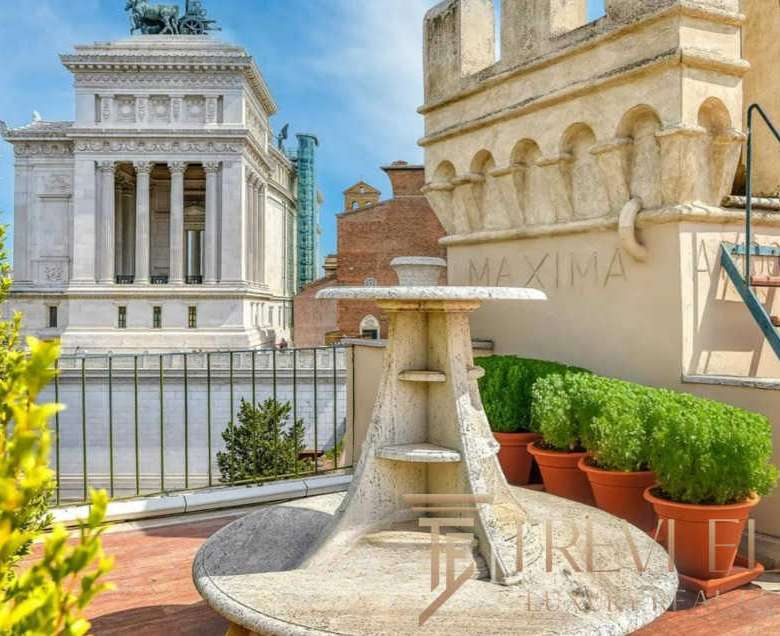 Элитный балкон с видом на архитектурные достопримечательности Рима, украшенный зеленью и уютной мраморной мебелью, идеальное место для отдыха и наслаждения городской атмосферой.