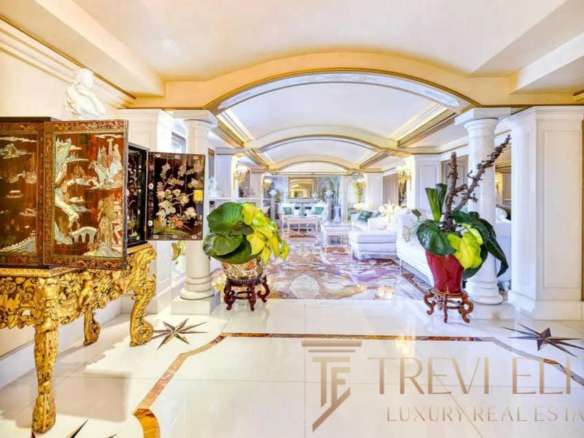 Роскошный интерьер роскошного дома с классическими элементами, белыми колоннами, золотой мебелью и зелеными растениями, создающими элегантную атмосферу.