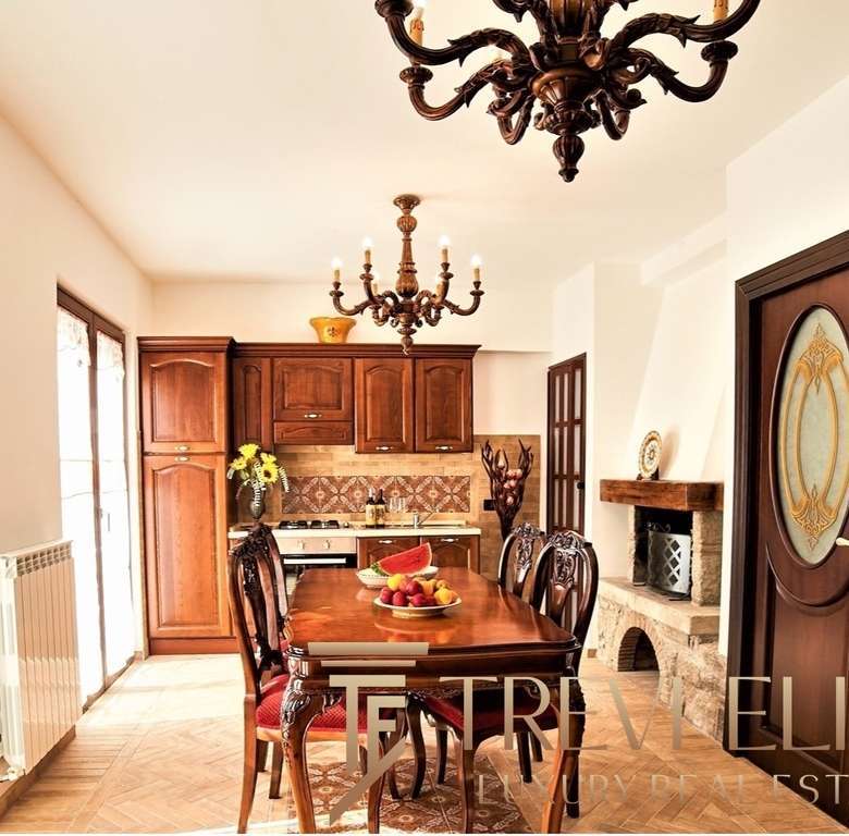 утрасолнечный интерьер с классической мебелью и камином в уютной кухне-столовой, деревянные шкафы и декоративные элементы, теплое освещение, стильное оформление для элитных недвижимости в Италии и мире.