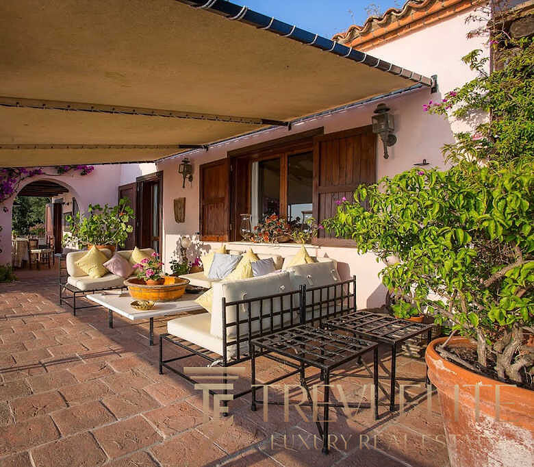 Элегантная терраса с уютной зоной отдыха на открытом воздухе, окруженная живописной зеленью и яркими цветами, идеально подходит для роскошного отдыха и развлечений.