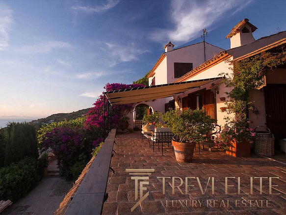 Уютный дом на холме с террасой, окружённый цветущими растениями и живописным видом на море и закат. Идеальное место для эксклюзивной недвижимости и спокойного отдыха.