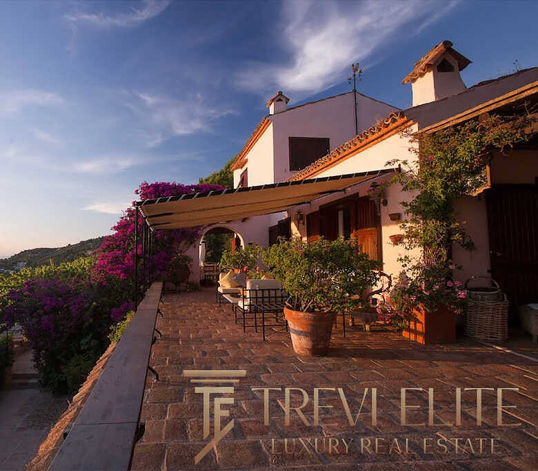 Уютный дом на холме с террасой, окружённый цветущими растениями и живописным видом на море и закат. Идеальное место для эксклюзивной недвижимости и спокойного отдыха.