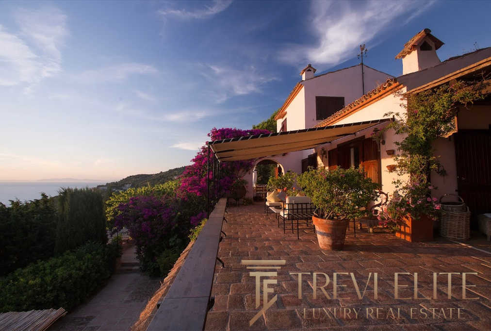 Уютный дом на холме с террасой, окружённый цветущими растениями и живописным видом на море и закат. Идеальное место для эксклюзивной недвижимости и спокойного отдыха.