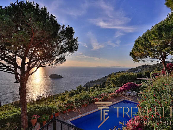 Узкий вид на бассейн и зеленый сад на фоне морского побережья во время заката, окруженный высокими деревьями и цветущими кустами, демонстрирующий роскошные особенности недвижимости Τреви Элит.