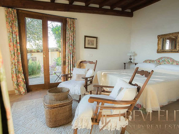 Уютная спальня с деревянной отделкой, зелёными видами на улицу через большие окна, изящной мебелью и романтическим декором, создающая атмосферу уютного дома.