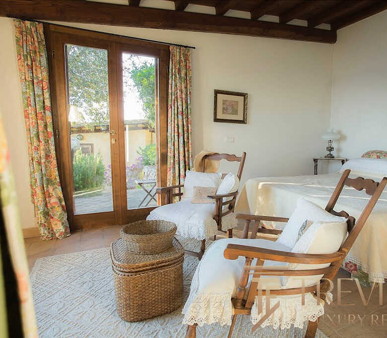 Уютная спальня с деревянной отделкой, зелёными видами на улицу через большие окна, изящной мебелью и романтическим декором, создающая атмосферу уютного дома.