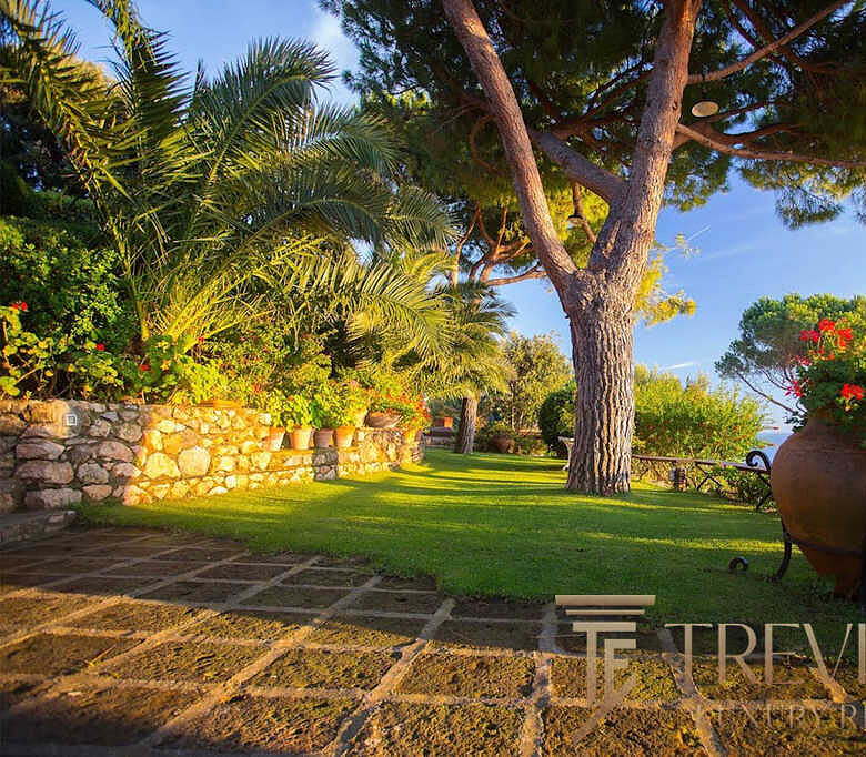 Изысканный сад с пышной зеленью и красивыми цветами у роскошного загородного дома на побережье, гармония природы и уединения.