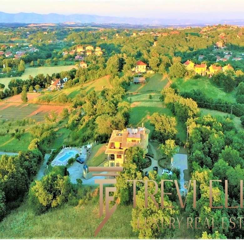 Вид на зеленую загородную местность с роскошным коттеджем и бассейном, окруженный деревьями и живописными пейзажами, привлекательный объект элитной недвижимости.
