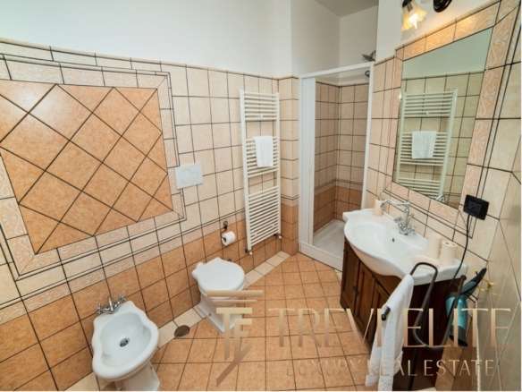 Современная уютная ванная комната с интерьером в теплых тонах, покрытая эстетичной керамической плиткой, включает зеркало, раковину, унитаз и биде для комфортного использования.