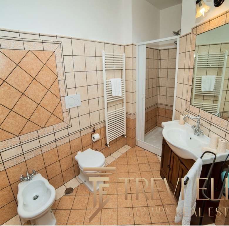 Современная уютная ванная комната с интерьером в теплых тонах, покрытая эстетичной керамической плиткой, включает зеркало, раковину, унитаз и биде для комфортного использования.