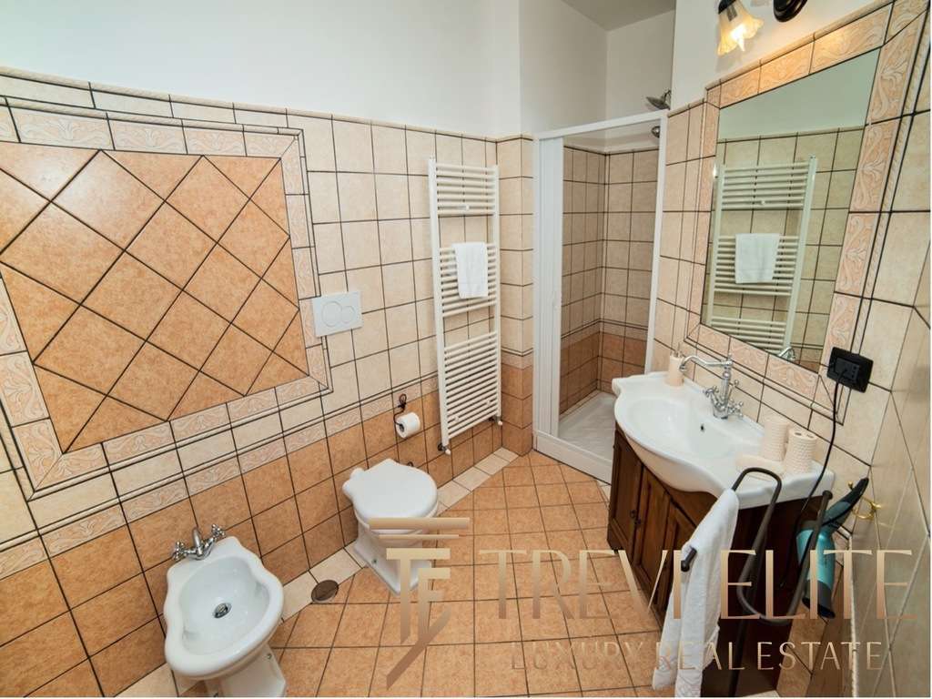 Современная уютная ванная комната с интерьером в теплых тонах, покрытая эстетичной керамической плиткой, включает зеркало, раковину, унитаз и биде для комфортного использования.