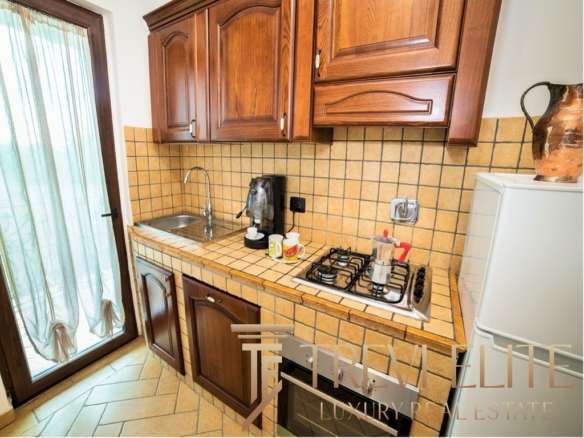 Угловая кухня с деревянными шкафчиками и плитой, рядом холодильник и окна с лёгкой шторой. Просторное и уютное пространство для кухни с современными аксессуарами и классическим стилем.