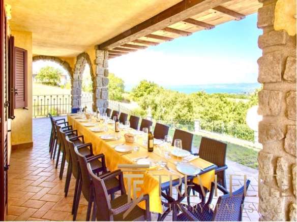 Уютный уличный обеденный стол на террасе с панорамным видом на природу и море, окруженный каменными колоннами и деревянной крышей, идеальное место для мероприятий на свежем воздухе.