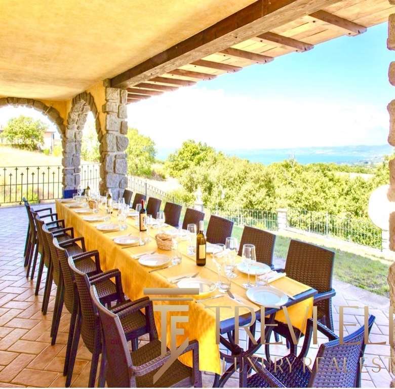 Уютный уличный обеденный стол на террасе с панорамным видом на природу и море, окруженный каменными колоннами и деревянной крышей, идеальное место для мероприятий на свежем воздухе.